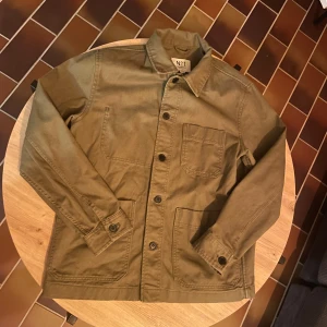 Mörkgrön overshirt  - Säljer en stilren overshirt med klassisk krage och tre stora fickor framtill. Jackan har knäppning med svarta knappar och är tillverkad i slitstark bomull. Perfekt för lager-på-lager och enkel att matcha med jeans eller chinos.