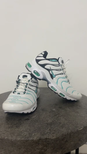 Nike TN vita och turkosa - Nike Air Max Plus sneakers i vitt med turkosa och svarta detaljer. Snyggt vågigt mönster på ovandelen, synliga Air-enheter i sulan och klassisk Tn-logga på hälen. Skorna har snörning, rund tå och platt sula. Ovandel i syntet och mesh för skön komfort.