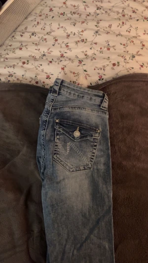 Blå Lågmidjade jeans  Nelly - Snygga blå jeans från Nelly med bootcut passform och klassisk femficksdesign. Jeansen har ljus tvätt, kontrastsömmar och knappstängning fram. Bakfickan har dekorativ söm och knapp. Perfekt för dig som gillar retrovibbar och avslappnad stil. Har små slitningar nere vid hälen men de syns inte. Priset är diskuterbart 