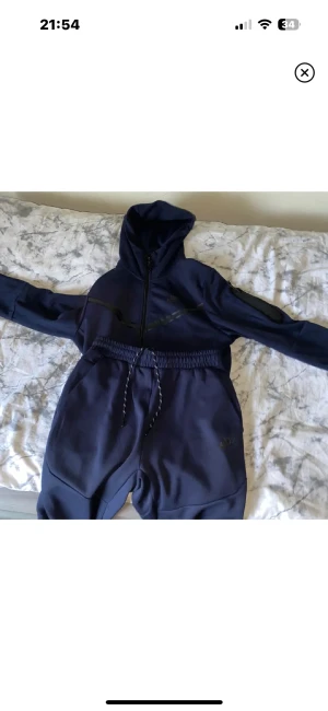 Marinblå Nike hoodie med dragkedja - Nike hoodie i marinblått med huva och hel dragkedja framtill. Snygga svarta detaljer och reflexband över bröstet. Tröjan har lång ärm och ribbad mudd vid ärmslut. Perfekt för träning eller chill. Materialet är mjukt och känns som polyester.