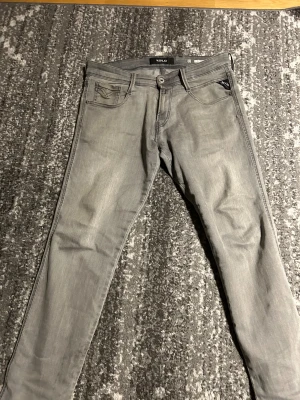 Grå Replay jeans slim fit - Snygga grå jeans från Replay med klassisk femficksdesign och diskreta sömmar på bakfickorna. Jeansen har smal passform och är tillverkade i mjukt denimtyg med stretch för extra komfort. Perfekta för dig som gillar stilrena och moderna byxor.