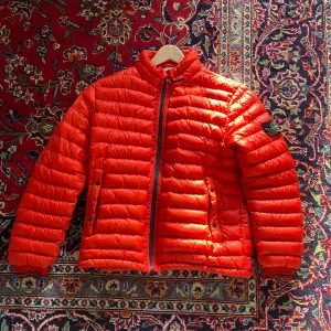 Orange pufferjacka från Stone Island - Säljer en dunjacka från stone island från 2013 (därav ingen QR-kod). Inte använd på ca 6 år. Har en flaw, se bild med patch. Storlek medium men sitter som en small. Pm för mer frågor