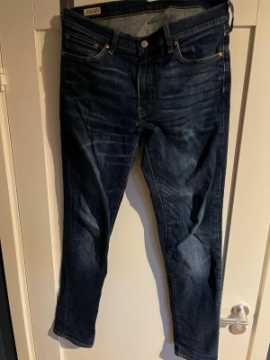 Levi's 511 mörkblå jeans - Säljer ett par Levi's 511 jeans i mörkblå tvätt med klassiska fem fickor, orangea nitar och snygga slitningar. Jeansen har en slim passform och raka ben, tillverkade i mjukt denimtyg. Perfekta för dig som gillar en stilren och tidlös look. W33 L34