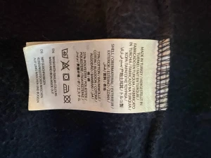 Mörkblå hoodie med dragkedja från GANT - Snygg mörkblå hoodie från GANT med vit logotyp framtill, dragkedja och snörning i huvan. Jackan har två fickor och är tillverkad i mjuk bomull och polyester. Perfekt för chill dagar och streetwear-stil.