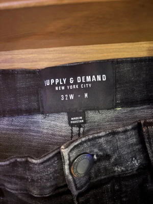 Supply & Demand svarta distressed jeans - Svarta jeans från Supply & Demand med coola slitningar, hål och vita färgstänk för en edgy look. Jeansen har dragkedja vid fickan och klassisk femficksdesign. Materialet är jeans och passformen är normal. Perfekt för dig som gillar streetstyle.