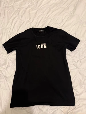 Svart DSQUARED2 ICON t-shirt XL - Svart t-shirt från DSQUARED2 i storlek XL med vit 'ICON' print på bröstet. Klassisk rund hals och korta ärmar. Tillverkad i mjuk bomull som känns skön mot huden. Snygg och stilren design som sticker ut med den feta loggan framtill.