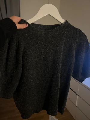 Mörkgrå stickad tröja Vero Moda - Säljer en mörkgrå stickad tröja från Vero Moda i storlek S. Tröjan har en rund halsringning och korta, puffiga ärmar som ger en cool siluett. Materialet är mjukt och lite luddigt, perfekt för dig som gillar en chill och trendig look.