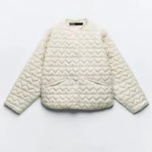 Quiltad vit pufferjacka från Zara - Säljer en quiltad pufferjacka från Zara i snygg vit färg. Jackan har lång ärm, rund hals och coolt mönster med hjärtformade och vågiga quiltningar. Stängs med knappar framtill och har två fickor. Perfekt för dig som gillar clean och trendig stil.