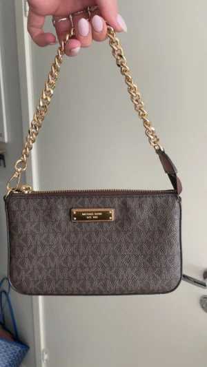  Michael Kors jet set väska - Perfekt söt festväska som passar till allt!! Så gott som ny då jag valde att köpa en annan väska och måste sälja en av dom… Väskan har MK-mönster över hela ytan, guldfärgad logoplatta och dragkedja upptill. Insidan är beige med fack för kort och detaljer i skinn. Perfekt storlek för det viktigaste.