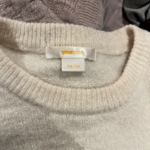 Beige stickad tröja Gina Tricot - Mysig beige stickad tröja från Gina Tricot i storlek 158/164. Tröjan har rund hals och ribbade muddar vid hals och nederkant. Enkel och stilren design som är lätt att matcha med olika outfits.