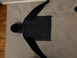 Marinblå colmar cardigan. - Marinblå cardigan jacka från Colmar med huva. Jackan har stickade ärmar, två dragkedjeförsedda fickor och en snygg, sportig look. Perfekt för kyliga dagar och har en modern passform. Insidan är slät och mjuk, med Colmar-logga i nacken och på axeln. Storlek 48 som översätter till en S/M. Nypris ca 3000kr.