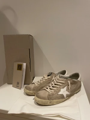 Golden Goose skor - Säljer nu mina snygga beige sneakers från Golden Goose. Skicket är bra på skorna, lite smutsiga bara. Samt heeldrag på höger skorn. Perfekta för dig som gillar en avslappnad och trendig look. Köpta för 5200 på nätet, så lär ha kvittot någonstans. 