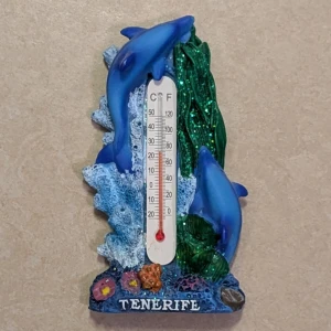 Magnet med termometer - Dekorativ kylskåpsmagnet med termometer, motiv av delfiner och havsbotten. Visar både Celsius och Fahrenheit. Färgglad design, souvenir från Tenerife. Magneten är hel och termometern fungerar. Mindre slitage på baksidan, annars i gott skick.