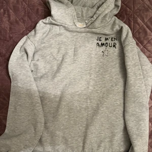 Grå hoodie från Gina Tricot med text - Grå hoodie från Gina Tricot med svart text 'JE M'EN AMOUR'. 