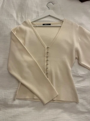 Beige kofta med knappar från Gina Tricot - Superfin gräddvit/beige kofta från Gina Tricot med v-ringning och dekorativa tygklädda knappar framtill. Långärmad och lätt figursydd modell i mjukt stickat material. Perfekt att styla med jeans eller kjol för en clean look. Använd några gånger men bra skick och inga defekter!! Ordinarie pris: 400kr