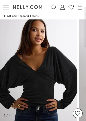 Svart omlottopp med v-ringning - Snygg svart omlottopp från Nelly med djup v-ringning och långa, lösa ärmar. Toppen har en croppad passform och är tillverkad i mjukt syntetmaterial som sitter skönt mot kroppen. Perfekt för dig som gillar stilrena och trendiga plagg.