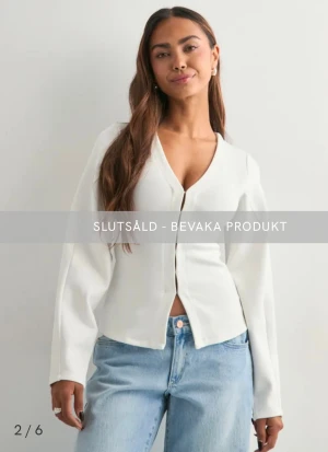 Vit v-ringad blus med knappar - Stilren vit blus med v-ringning och långa ärmar. Modellen är figurnära upptill och har en lätt utsvängd nederkant. Blusen har knäppning framtill och är tillverkad i ett slätt, mjukt material som ger en clean look.