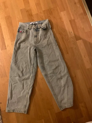 Big Boy ljusgrå - Säljer ett par ljusgrå jeans från Big Boy med bred passform och hög midja. Klassisk femficksdesign, blå patch med logga bak och en liten röd patch fram. Jeansen är tillverkade i jeansmaterial och har raka, vida ben för en avslappnad look.