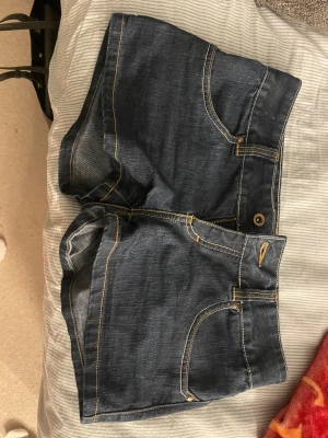 Mörkblå jeansshorts med fickor - Snygga mörkblå jeansshorts med klassisk femficksdesign och kontrasterande gula sömmar. Modellen är tight och har knapp och dragkedja framtill. Perfekta för varma dagar och passar till allt. Materialet är bomull med lite stretch för skön passform. Midjemått 38