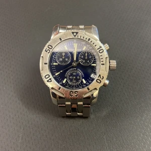 Tissot PRS200 kronograf herrklocka - Snygg Tissot PRS200 kronograf med blå urtavla och silverfärgat armband i metall. Klockan har flera subdials, tydliga siffror på boetten och robust länkarmband med lås där PRS200 är ingraverat. Perfekt för dig som gillar sportig och stilren design.