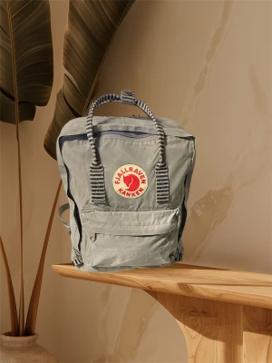 Grå Fjällräven Kånken ryggsäck - Säljer en klassisk grå Fjällräven Kånken ryggsäck med ikonisk rund röd logga framtill. Väskan har randiga handtag och axelremmar, en stor huvudficka med dragkedja och en mindre ficka framtill. Materialet är slitstark syntet och designen är fyrkantig och praktisk.