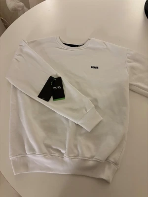 Vit sweatshirt från Hugo Boss, storlek S - Vit sweatshirt från Hugo Boss, Den är i storlek S riktigt fin! Men den har en liten fläck på ryggen som syns på bild 4, Men det borde gå bort med vanish eller nått liknande.