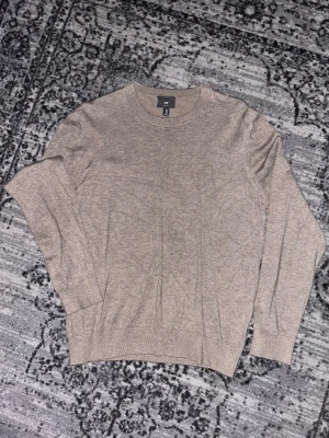Beige stickad tröja från H&M - Snygg beige stickad tröja från H&M i slim fit-modell. Tröjan har rund halsringning och långa ärmar med ribbade muddar vid ärmslut och nederkant. Perfekt för dig som gillar enkel och stilren design.