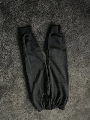 Mörkgrå mjukisbyxor med snörning 158-168 - Säljer ett par mörkgrå mjukisbyxor med elastisk midja och snörning. Byxorna har ribbade muddar vid bensluten och är gjorda i mjukt material, perfekta för chill dagar. Klassisk passform och stilren look.