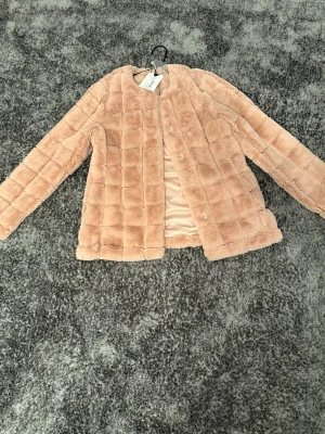 Ljusrosa pälsjacka från Visual Clothing Project - Säljer en supermjuk ljusrosa pälsjacka från Visual Clothing Project i storlek S. Jackan har ett rutigt quiltat mönster, rund hals och knappar framtill. Materialet är fuskpäls med slät insida i satin. Perfekt för dig som vill ha en cozy och stylish look. Den är helt oanvänd prislappen står kvar.     Priset är ej 100% satt