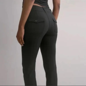 Svarta kostymbyxor med bootcut - Svarta bootcut kostymbyxor. Byxorna har tvà bakfickor med knappdetaljer och stängs med en dragkedja och knappar framtill