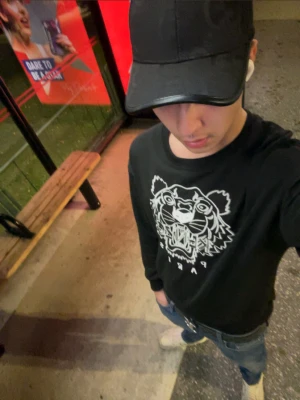 Svart Kenzo hoodie med tigertryck - Svart hoodie från Kenzo med ikoniskt vitt tigertryck på bröstet och texten 'Paris' under motivet. Klassisk passform med ribbade muddar och rundad hals. Materialet är mjukt och bekvämt, perfekt för en chill och stilren look.