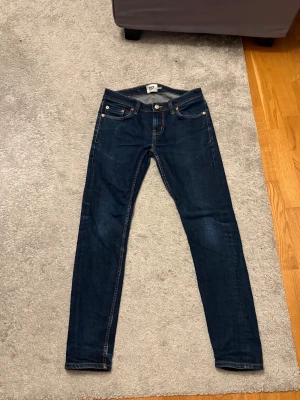 Mörkblå skinny jeans från 157, S - Snygga mörkblå jeans från 157 i storlek S. Modellen är skinny med klassisk femficksdesign, kontrastsömmar och läderpatch bak i midjan. Jeansen har normal passform och är tillverkade i mjukt denimtyg med dragkedja och knapp framtill. Perfekt till skolan och när man vill vara lite stilig i vardagen 