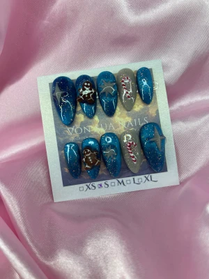 Noel (S);Medium Almond - Set med handgjorda press-on naglar i cateyemetallicblått med glitter, dekorerade med handgjorda 3D pepparkaksgubbe, stjärnor och polkagrisar. Några naglar är gråa med julmotiv. Naglarna är medium långa och har en almond form, perfekt för dig som vill sticka ut under vintern.S: 15 mm, 11,5 mm, 12 mm, 11 mm, 9 mm 