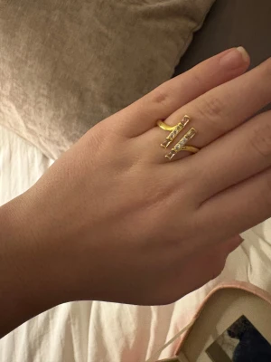 Guldfärgad ring med glittriga stenar - Snygg guldfärgad ring med två parallella stavar dekorerade med glittriga stenar. Modern och stilren design som ger en cool touch till din look. Perfekt för dig som gillar att sticka ut med detaljer.