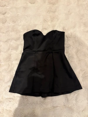 Svart bustier topp från STOCKH LM Studio - Supersnygg svart bustier topp från STOCKH LM Studio i satinliknande polyester. Topen är axelbandslös och har en markerad midja med lätt utsvängd nedre del. Helt oanvänd 