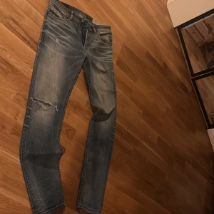 Diesel jeans - Snygga vintage diesel jeans i blå tvätt med slitningar och en trasig detalj på vänster ben. Tapered fit med klassiska fem fickor och dragkedja. Materialet är mjukt och stretchigt jeans, perfekt för en avslappnad stil.