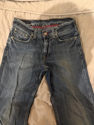 Blå jeans från Tommy Hilfiger 31/34 - Snygga blå jeans från Tommy Hilfiger med klassisk femficksdesign och kontrastsömmar. Jeansen har en rak passform och är tillverkade i slitstarkt denim med diskret logodetalj på fickorna. Perfekt för dig som gillar stilrena och tidlösa jeans.
