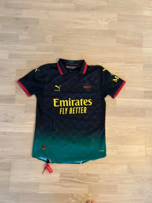 AC Milan x Off-White x Puma fotbollströja M - Snygg AC Milan fotbollströja i samarbete med Off-White och Puma. Tröjan är svart med grönt nedtill, har gula tryck och röda detaljer vid krage och ärmslut. Kortärmad med diskret mönster och klassisk krage. Det är PRO version som är slut sold hos Milan och Puma. 