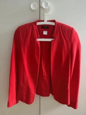 Röd kavaj från La Redoute - Snygg röd kavaj med rak passform och stilren design från Redoute Collection. Jackan har lång ärm, öppen front utan knappar och diskreta fickor framtill. Materialet är tillverkad i ett strukturerat tyg som ger en modern känsla. Perfekt för att lyfta alla outfits men din fina färg. Kavajen är i storlek US 4