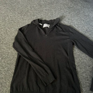 Grå polotröja med dragkedja från Selected Homme - Mörkgrå polotröja från Selected Homme med halv dragkedja i halsen. Tröjan har långa ärmar och är tillverkad i ett mjukt material som passar perfekt till lager-på-lager. Enkel och stilren design.