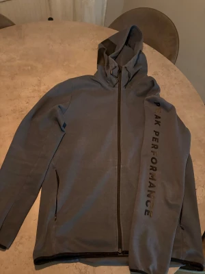 Gråblå tröja Peak Performance - Snygg gråblå tröja från Peak Performance med svart logga på huvan i storlek L 