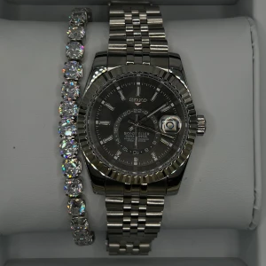 Seiko Sky-Dweller automatisk herrklocka - Snygg Seiko Sky-Dweller herrklocka med automatisk urverk och robust länkarmband i silverfärgat metall. Urtavlan är mörkgrå med tydliga index och datumfönster med förstoringsglas. Klockan har en rund form och klassisk bezel med räfflad kant.