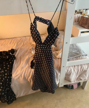 Svart prickig kortklänning från Zara - Supersöt svart klänning från Zara med rosa prickar, smala axelband och snygg v-ringning. Klänningen har en kort längd och ärmlös design med ett elastiskt band i ryggen för extra komfort. Perfekt för dig som gillar trendiga och lekfulla plagg.