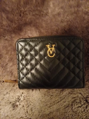 Svart plånbok från Valentino (fejk) - Snygg svart plånbok från Valentino med  guldfärgade detaljer. Plånboken har ett V-logo framtill, dragkedja runt myntfacket och flera kortfack på insidan. FEJK!