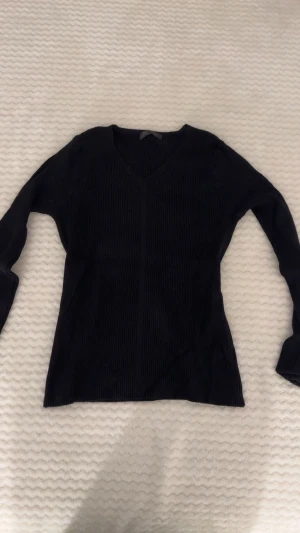 Svart ribbad stickad tröja från Dazy - Svart långärmad stickad tröja från Dazy i storlek M. Tröjan har en snygg v-ringad hals och är ribbad för extra stilpoäng. Perfekt för dig som gillar enkel men trendig design. Passar dig som vill ha en klassisk svart tröja med lite edge.