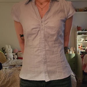 Ljusblå kortärmad skjorta - Ljusblå skjorta med korta ärmar och v-ringad hals. Subtilt randigt mönster i tyget och är figurnära i passformen. Starkare blå än på andra bilden.