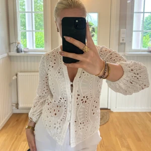 Vit broderad blus med knappar - Superfin vit blus i bomull med broderade blommönster och hålbroderier. Långärmad modell med v-ringning, knappar framtill och lätt puffade ärmar med resår vid handlederna. Storlek M men sitter som en S.💖💖
