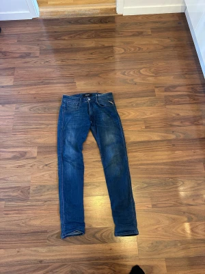 Replay Anbass blå jeans, stl 31/32 - Snygga blå Replay Anbass jeans i klassisk tvätt med smal passform. Jeansen har fem fickor, dragkedjegylf och diskreta slitningar för en cool look. Perfekta för dig som gillar stilrena och moderna jeans med bekväm känsla.
