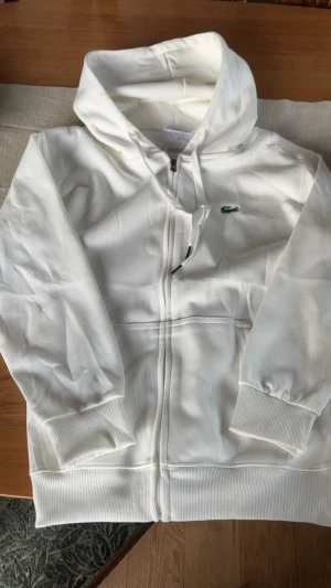Lacoste zip up - Vit Lacoste zip i storlek S, ny med lappar, endast testat. Hör av er med frågor eller liknande.