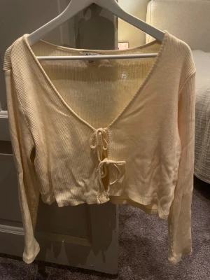 Beige ribbad topp från Monki - Säljer min beigea långärmade topp från Monki i storlek M. Toppen stängs med två knyten framtill och passar perfekt över ett linne eller bikini. Jag säljer den då jag har för många liknande toppar!❣️ 